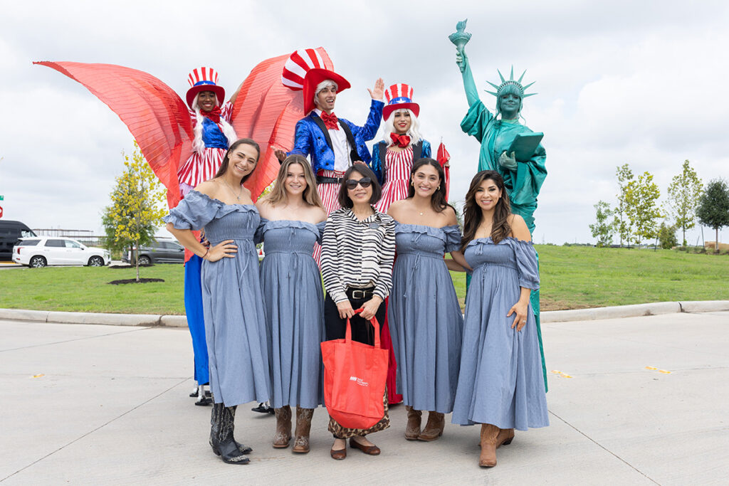 Group photo at Brookewater event near Richmond TX: women in blue dresses, stilt walkers, and Statue of Liberty.