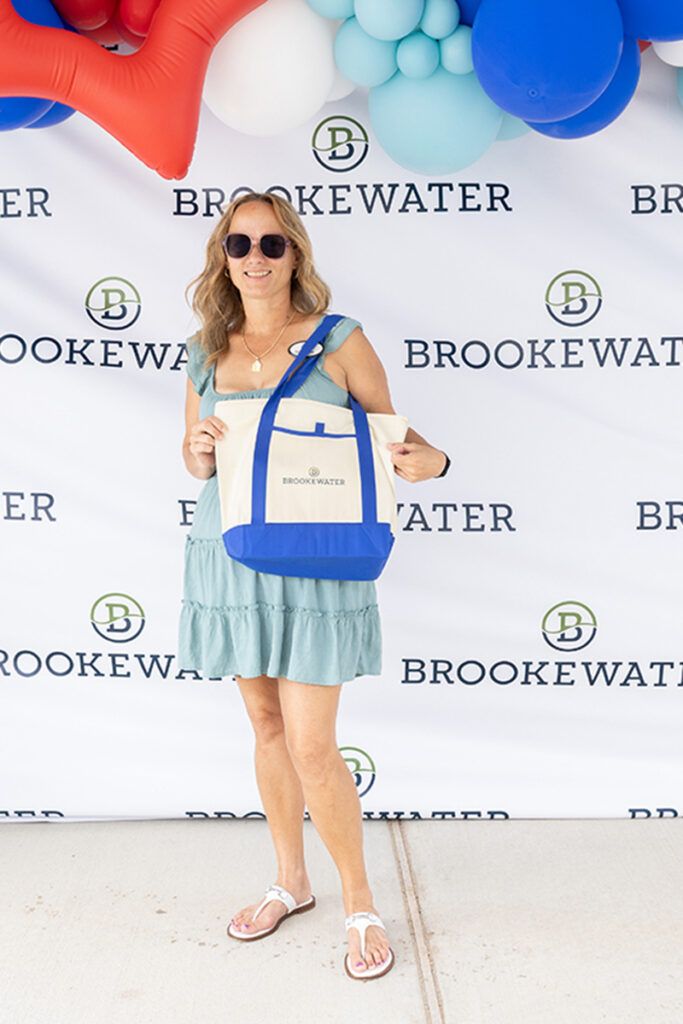 Woman in sunglasses with a Brookewater tote stands before a master-planned community backdrop.