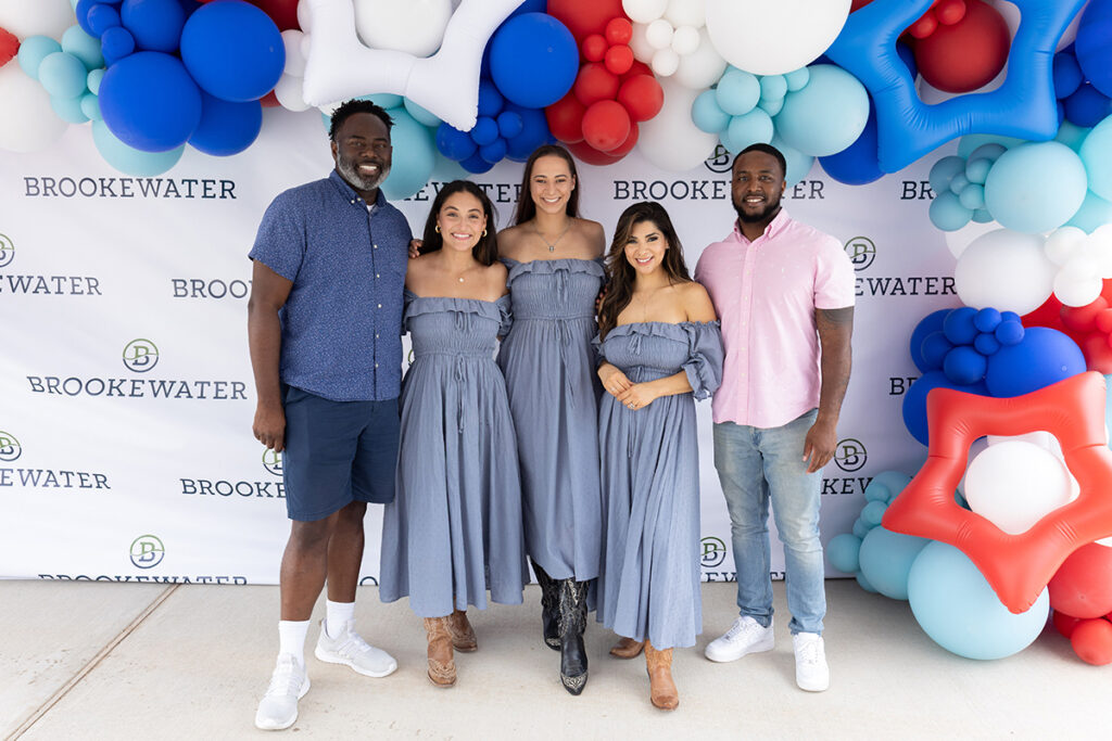 Five people pose near Richmond TX in front of a Brookewater backdrop with festive balloon decorations.