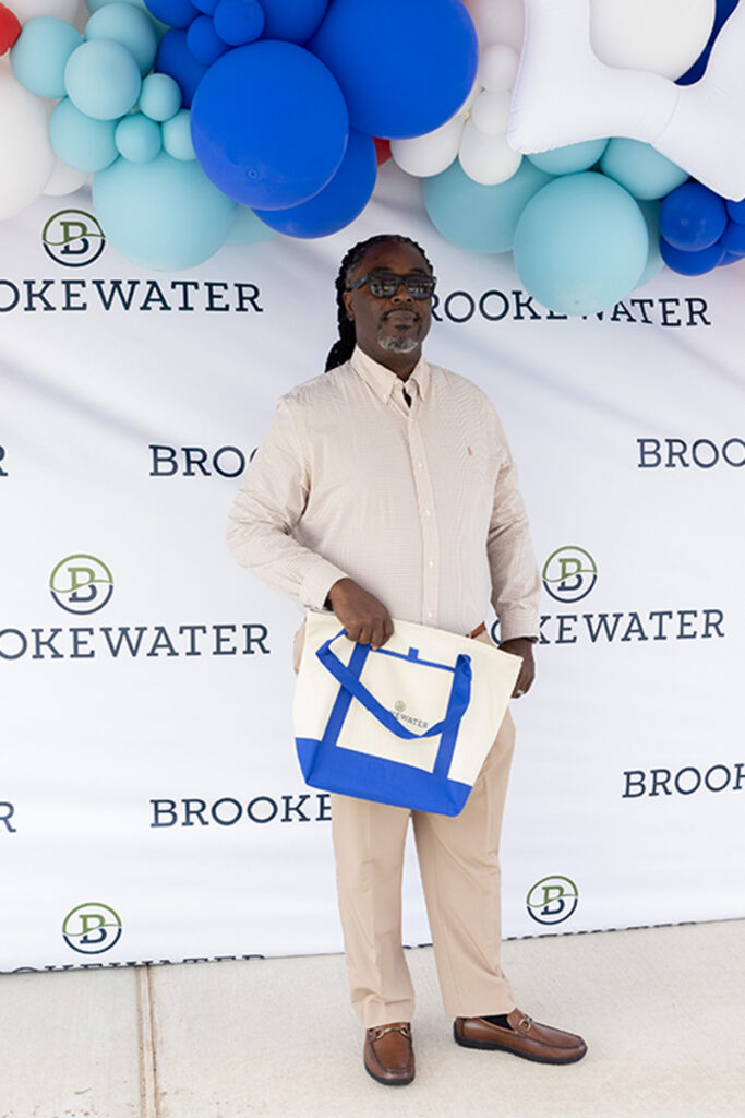 Man stands before a Brookewater backdrop, showcasing a blue tote near new homes for sale.