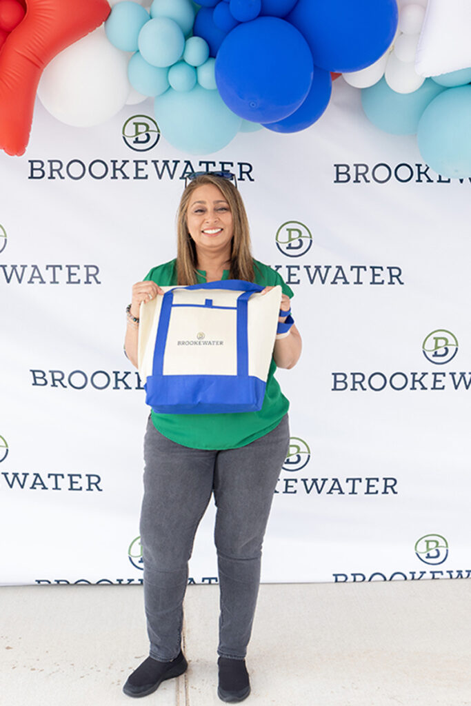 Woman holding a Brookewater tote bag at a master-planned community event backdrop.