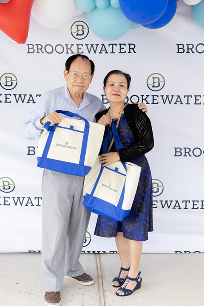 Two people hold Brookewater tote bags at a master-planned community branded backdrop.