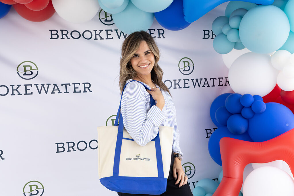 Woman holding a Brookewater tote bag stands near Richmond TX in front of a balloon backdrop.