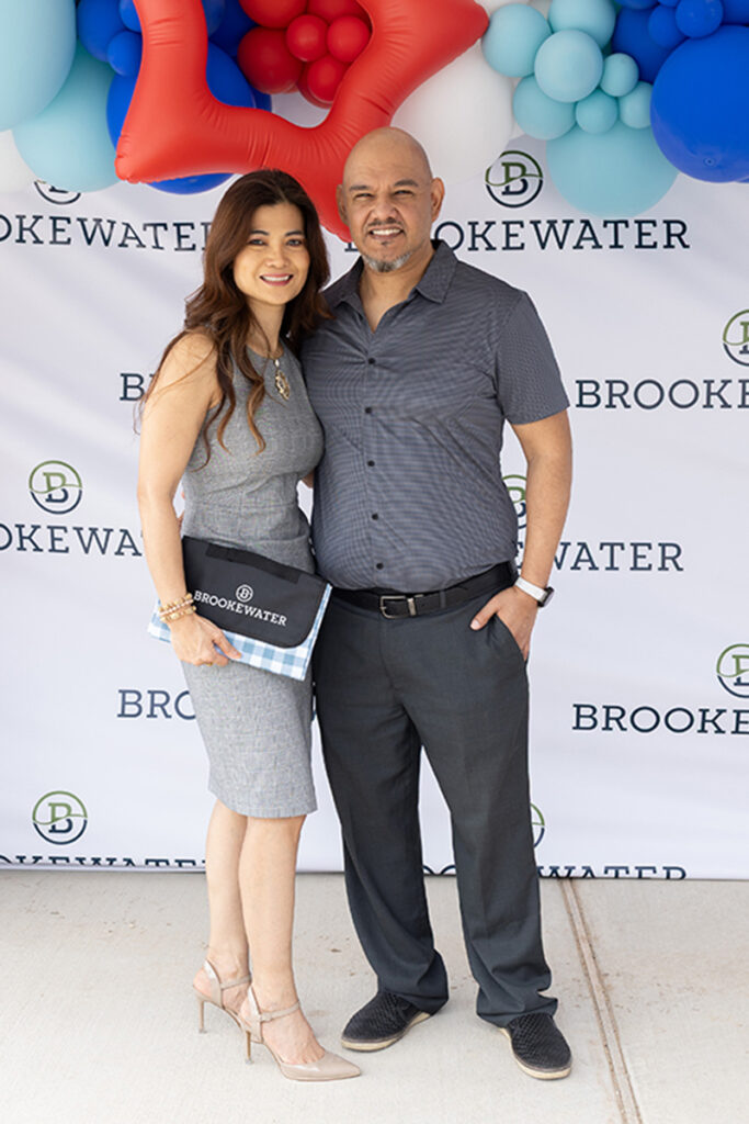 Two people pose in front of a Brookewater master-planned community backdrop with balloons overhead.