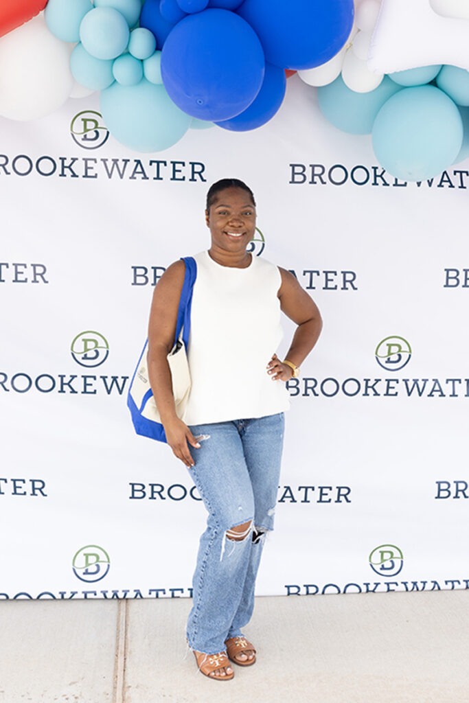 A woman poses at Brookewater near Richmond TX with blue and white balloons above.
