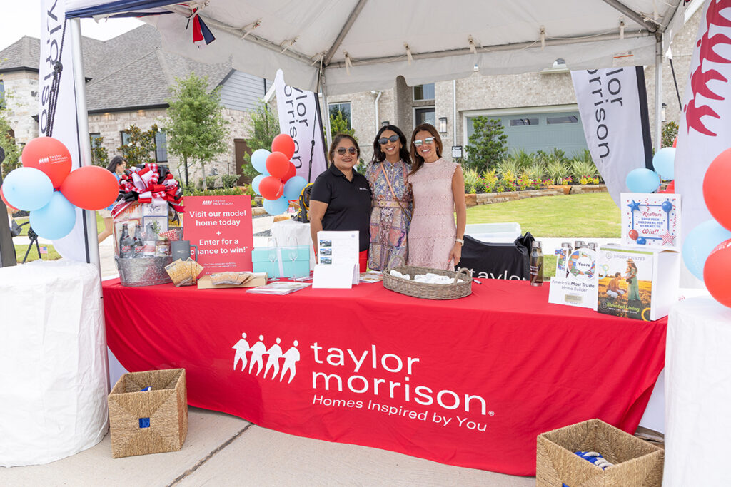 A group of women stand near Richmond TX in front of a table with a red tablecloth. Brookewater event.