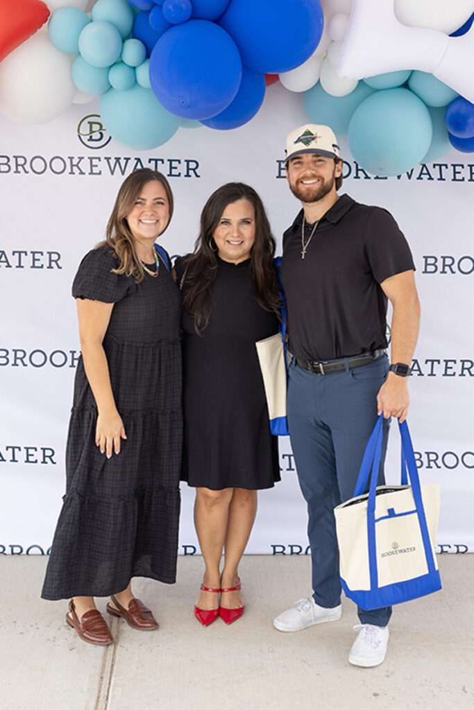 Three people smile with tote bags before a Brookewater backdrop, near Richmond TX.
