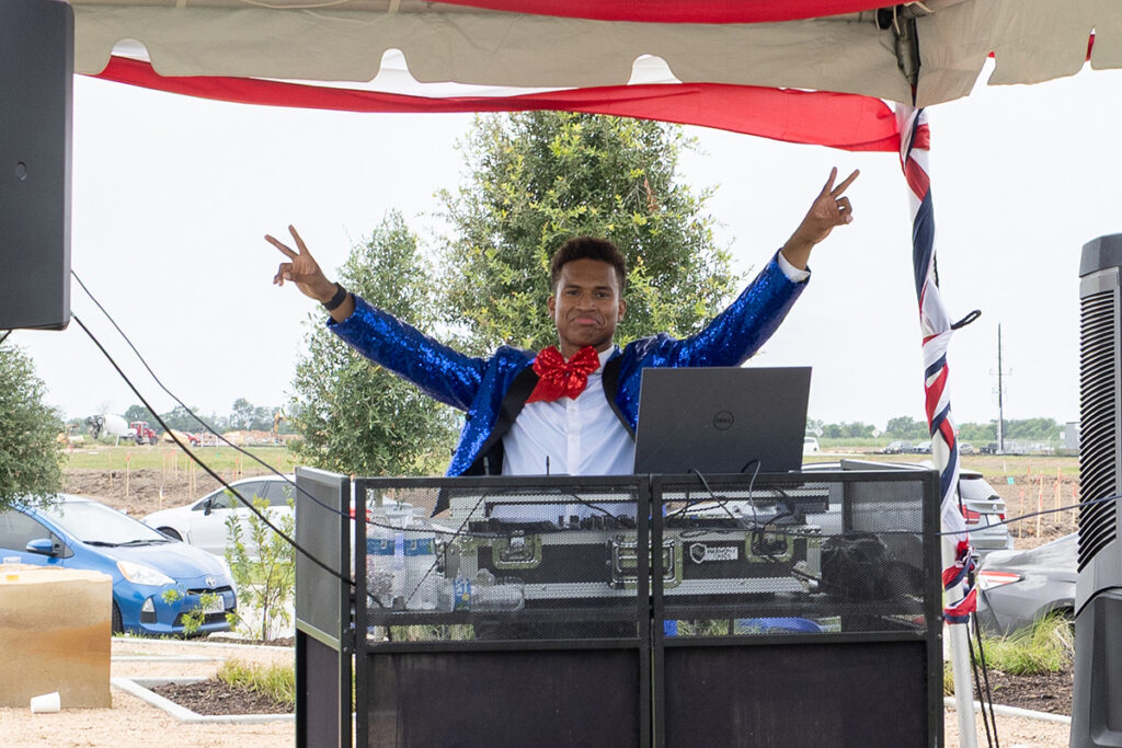 Person in a blue sequin jacket DJs near Richmond TX, raising both hands in a peace sign at a Brookewater event.