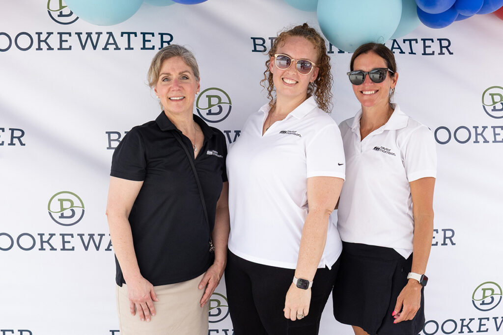 Three women smile by a Brookewater backdrop, celebrating new homes for sale near Richmond TX.