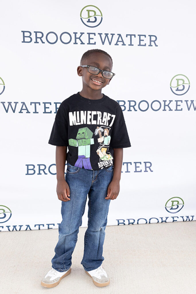 Smiling boy in glasses and Minecraft shirt stands by a Brookewater backdrop near Richmond TX.