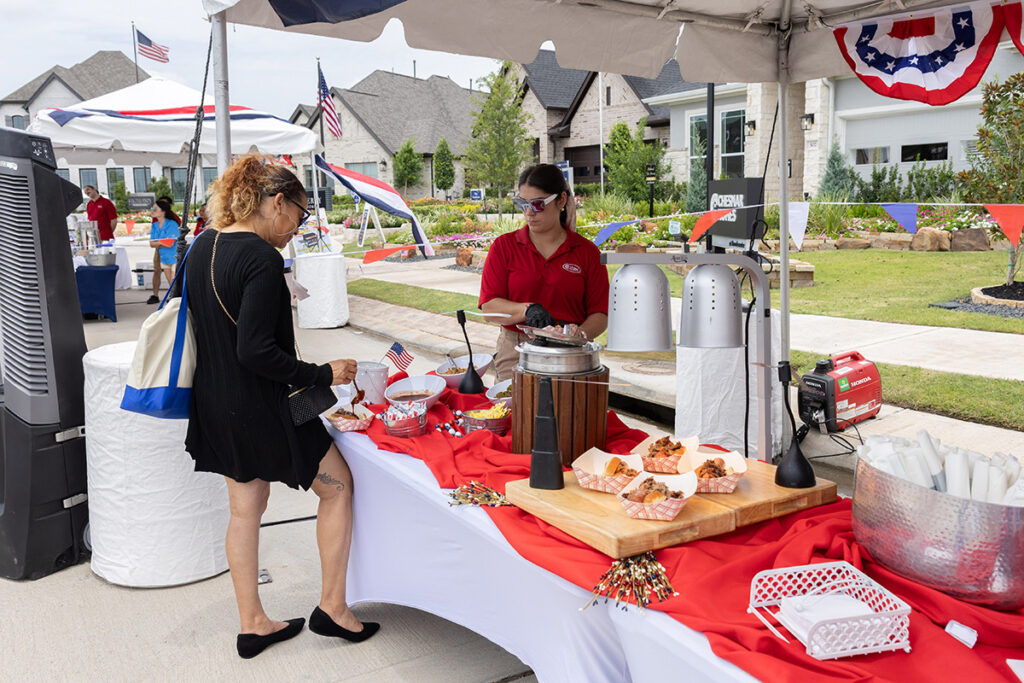 A woman is served food at an outdoor booth near Richmond TX, decorated with red, white, and blue. Brookewater event.