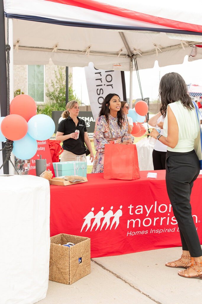 People gather at a Taylor Morrison booth, new home builders near Richmond TX, with balloons and bags.