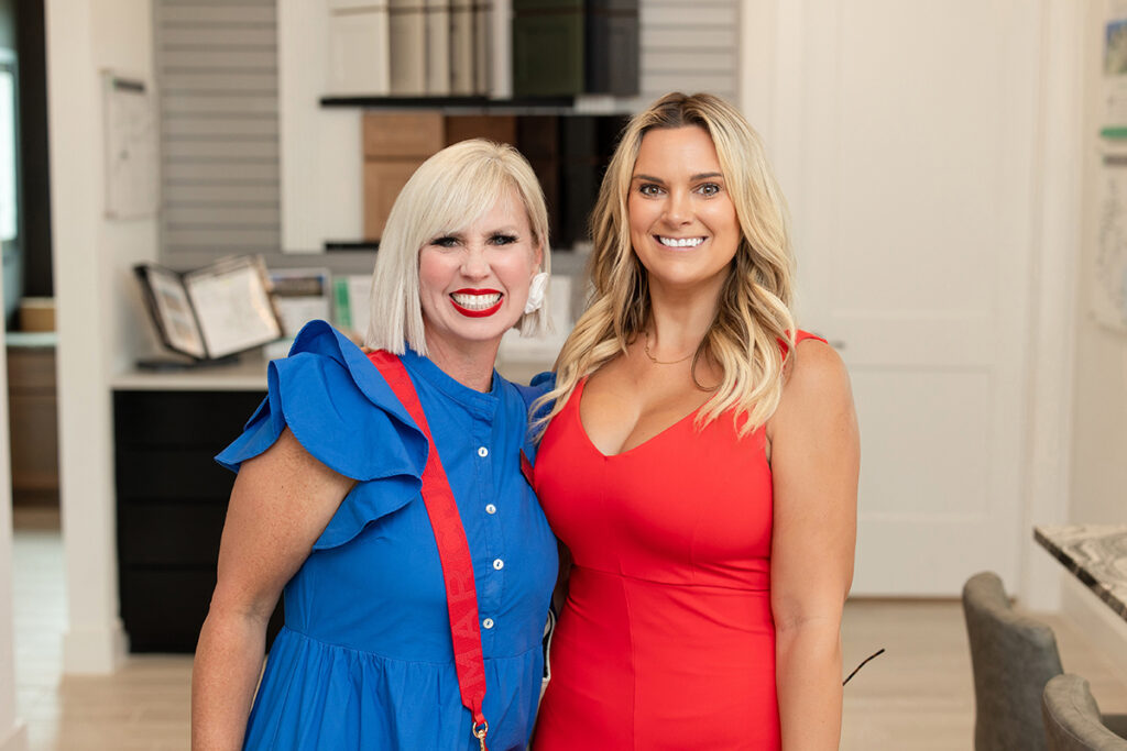 Two women smiling indoors, chatting about new at Brookewater homes for sale, standing side by side.