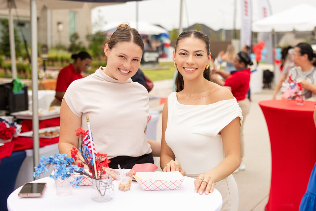 Two women chat at a food table during a Brookewater new homes for sale event outdoors.