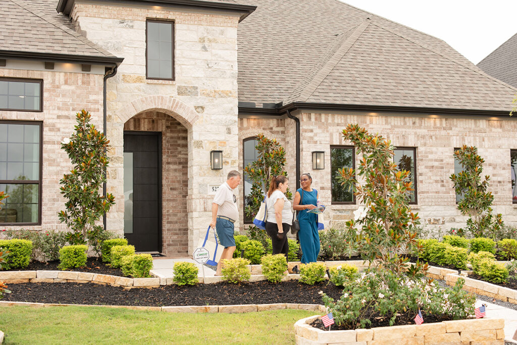 Three people talk outside a two-story brick house built by new home builders near Richmond TX at Brookewater.