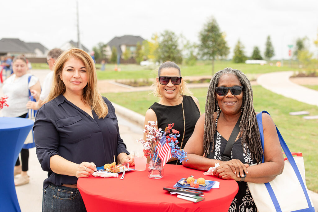 Three women gather at a red table with food and drinks near Richmond TX at Brookewater event.