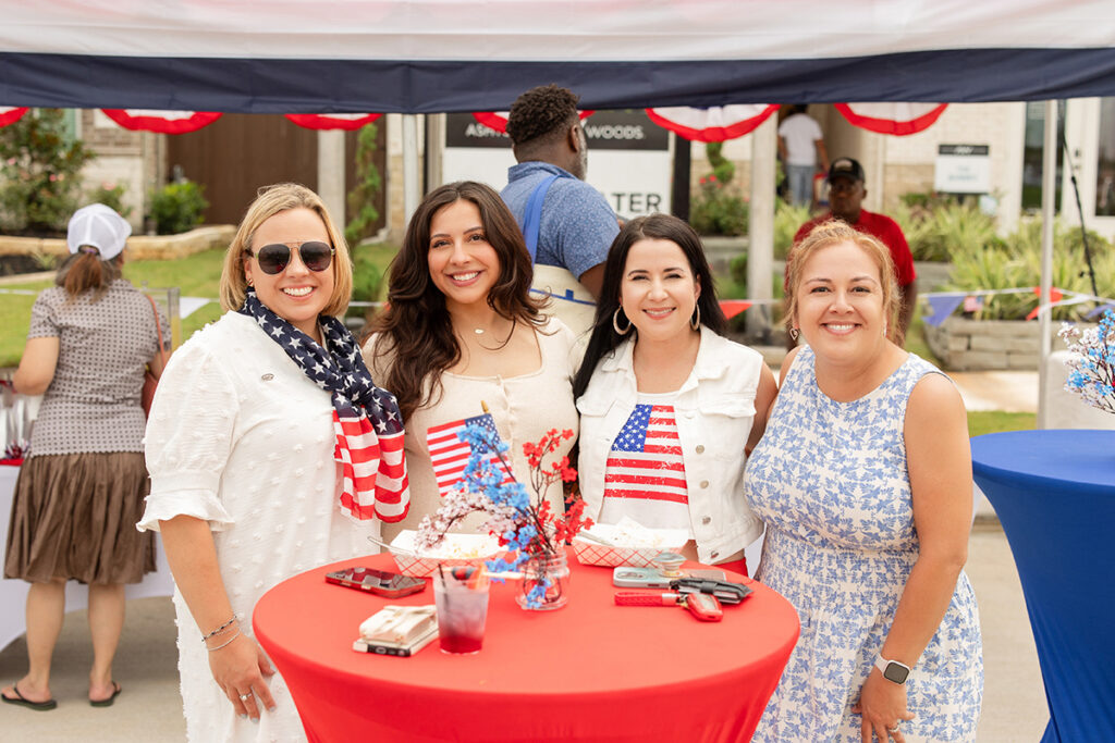 Four women in patriotic attire stand around a red table near Richmond TX at an outdoor Brookewater event.