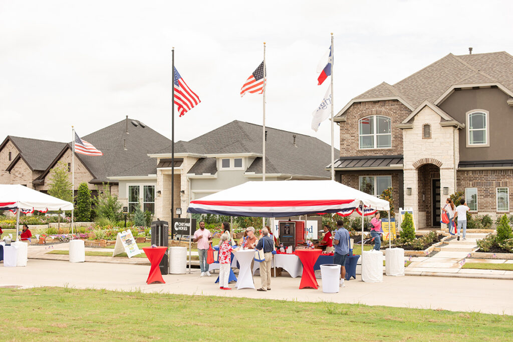 People gather at outdoor tents at Brookewater near Richmond TX, American flags waving above new homes for sale.