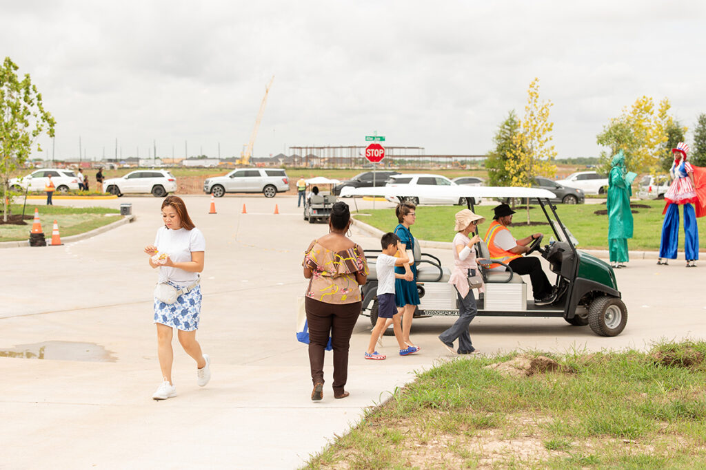People walking and a golf cart in a parking lot at Brookewater new homes for sale near Richmond TX.