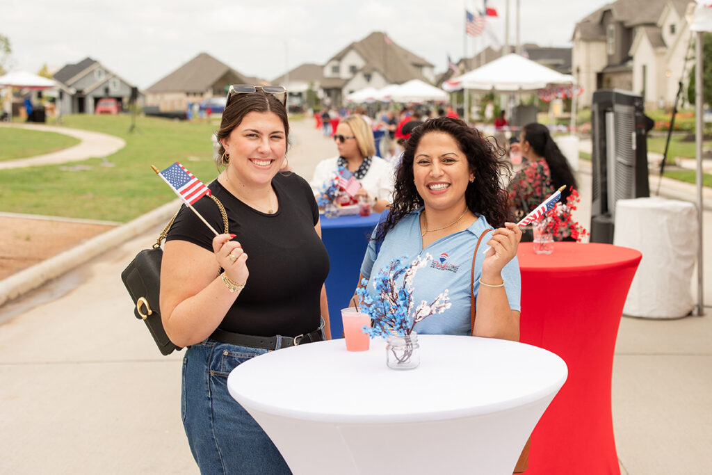 Two women at a Brookewater event hold flags, celebrating this master-planned community.