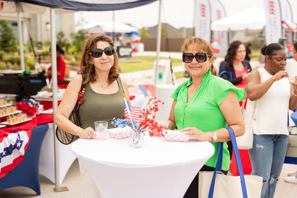 Two women with sunglasses enjoy a festive table at a Brookewater master-planned community event.