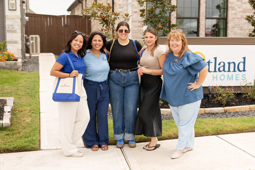 Five women smile together by a sign, showcasing Brookewater new homes for sale.