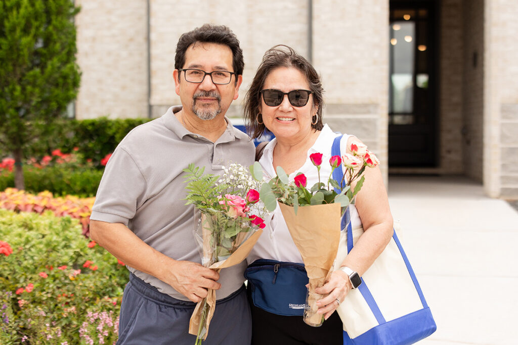 Two adults at Brookewater smile outside, holding bouquets in Brookewater, a master-planned community.