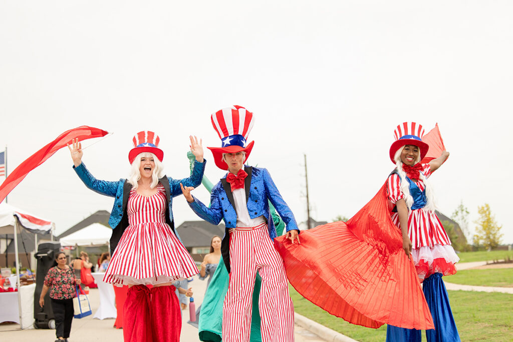 Three people in patriotic costumes pose and wave at an outdoor Brookewater event near Richmond TX.