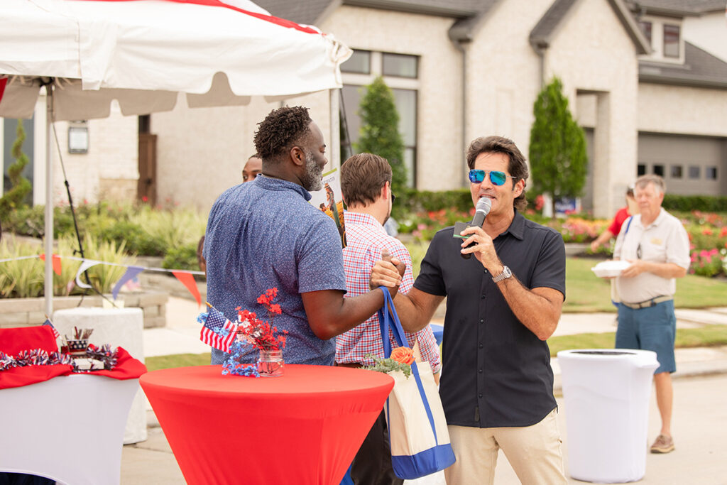 A man speaks into a microphone at an outdoor Brookewater event near Richmond TX with decorated tables.
