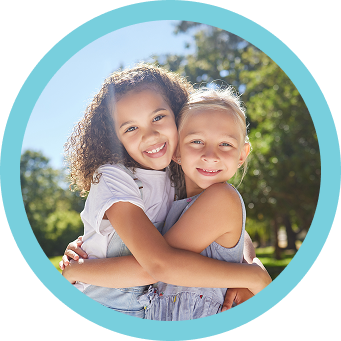 Two children hugging and smiling outdoors, framed by a blue circle in a master-planned community.