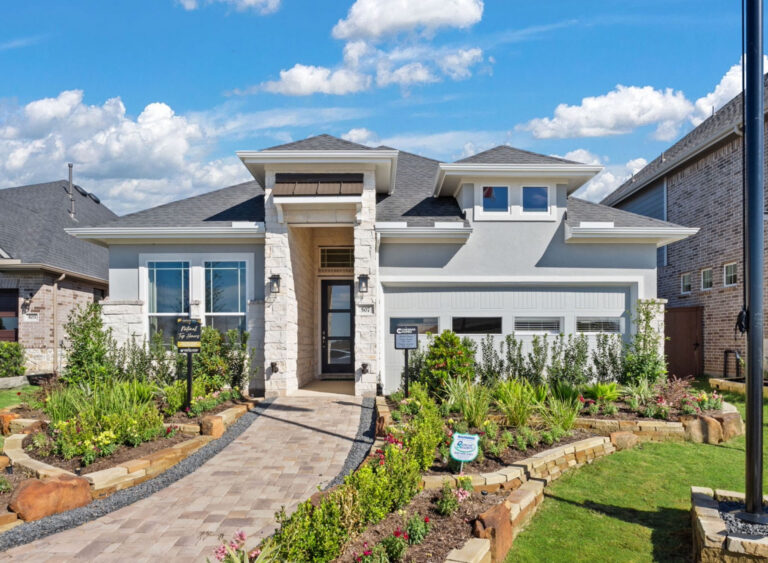 Modern single-story house with stone accents, landscaped yard, and paved walkway under blue sky.