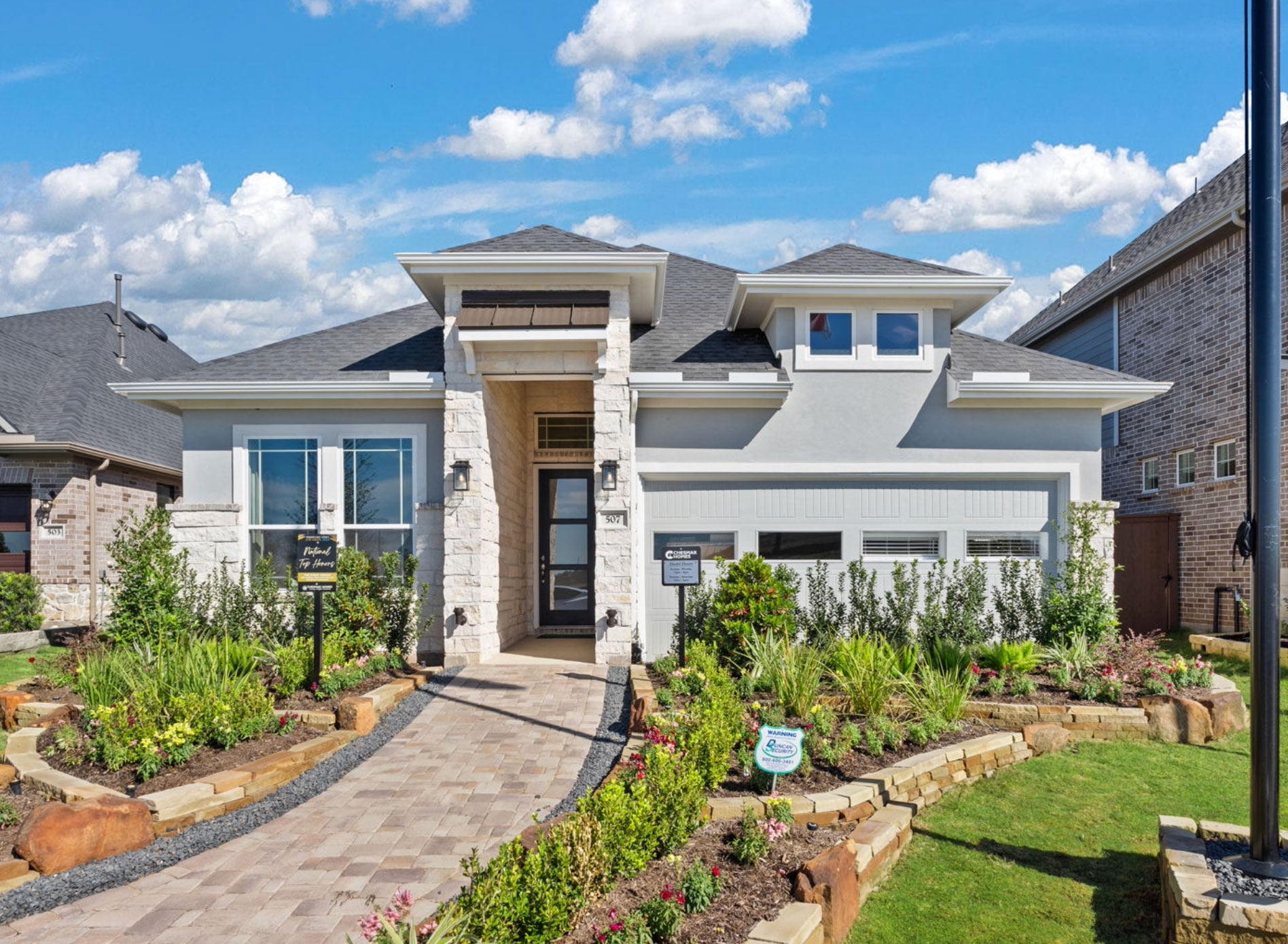 Modern single-story house with stone accents, landscaped yard, and paved walkway under blue sky.