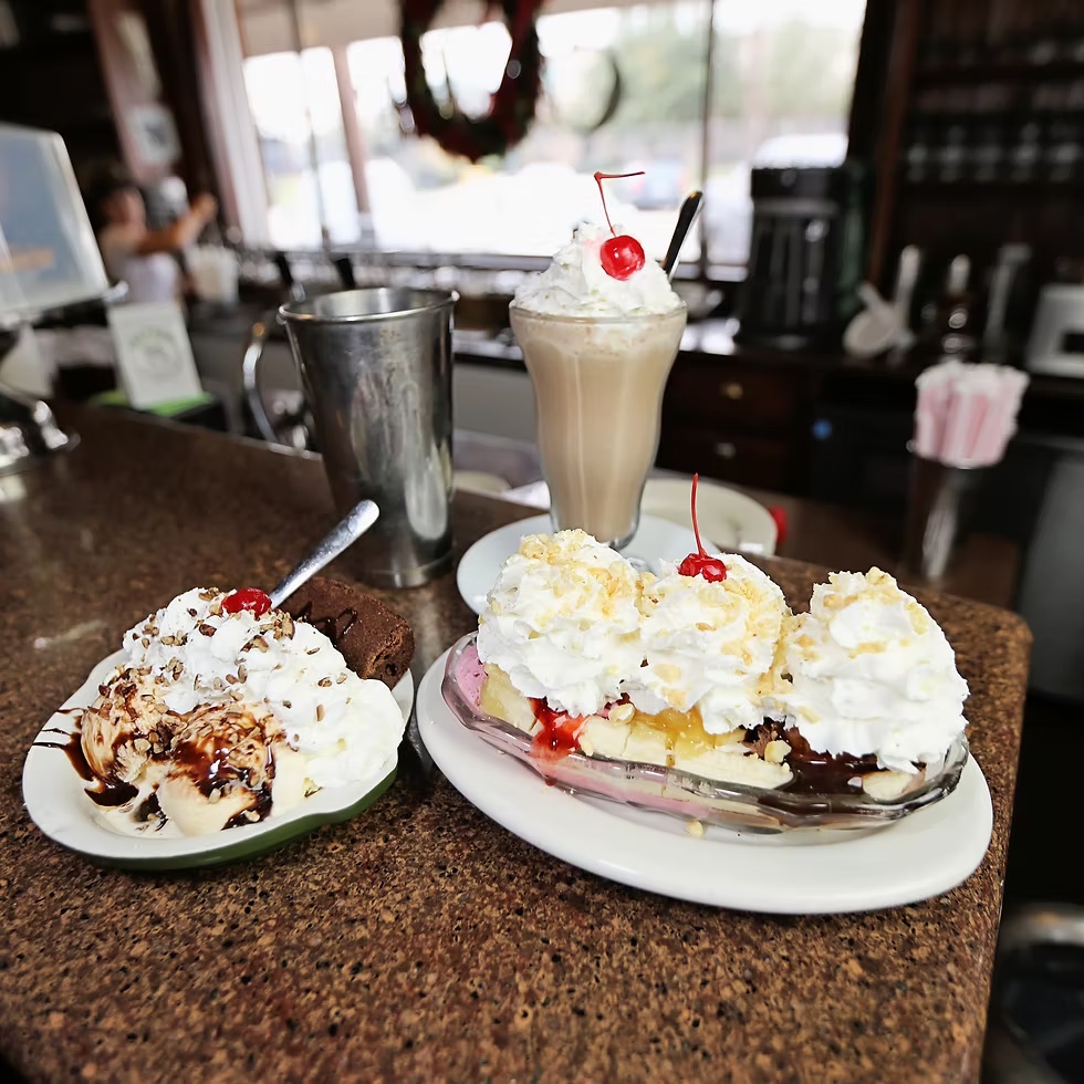 Ice cream sundae, banana split, and milkshake with whipped cream and cherries on a diner counter.