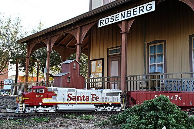Model Santa Fe train on tracks in front of the Rosenberg train station building.