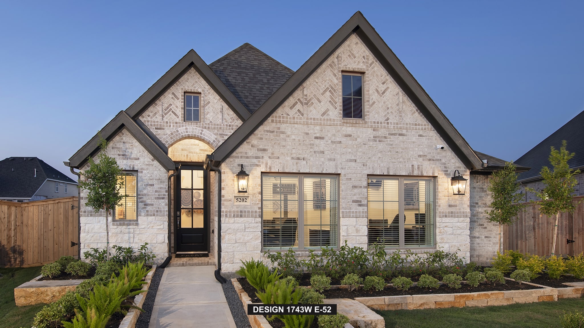 Single-story brick house with dark roof, front garden, and large windows at dusk.